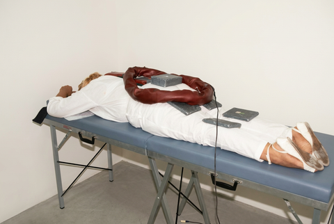 Person lying face down on a treatment table with magnetic-field equipment positioned over the body