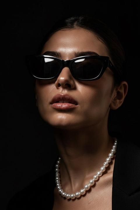 A close-up portrait of a woman a white pearl magnetic necklace against a dark black background.