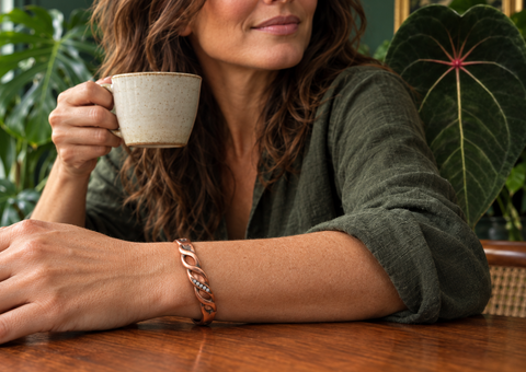 Mujer tomando café con pulsera de cobre y plantas al fondo