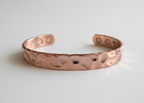 A hammered copper cuff bracelet with a hammered texture and circular cutouts on the ends, displayed on a light gray background.