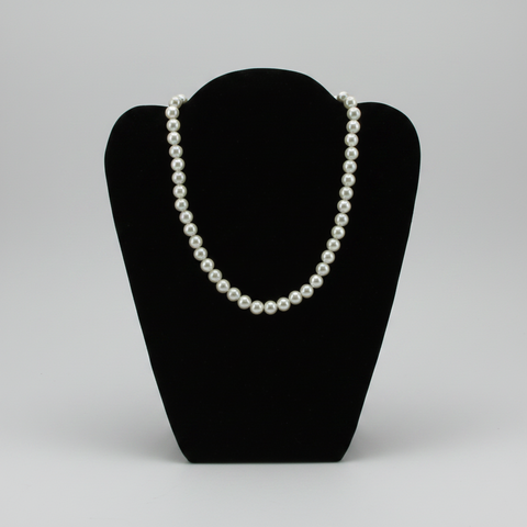 A classic pearl necklace displayed on a black velvet jewelry bust against a neutral gray background.