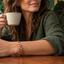Mujer tomando café con pulsera de cobre y plantas al fondo